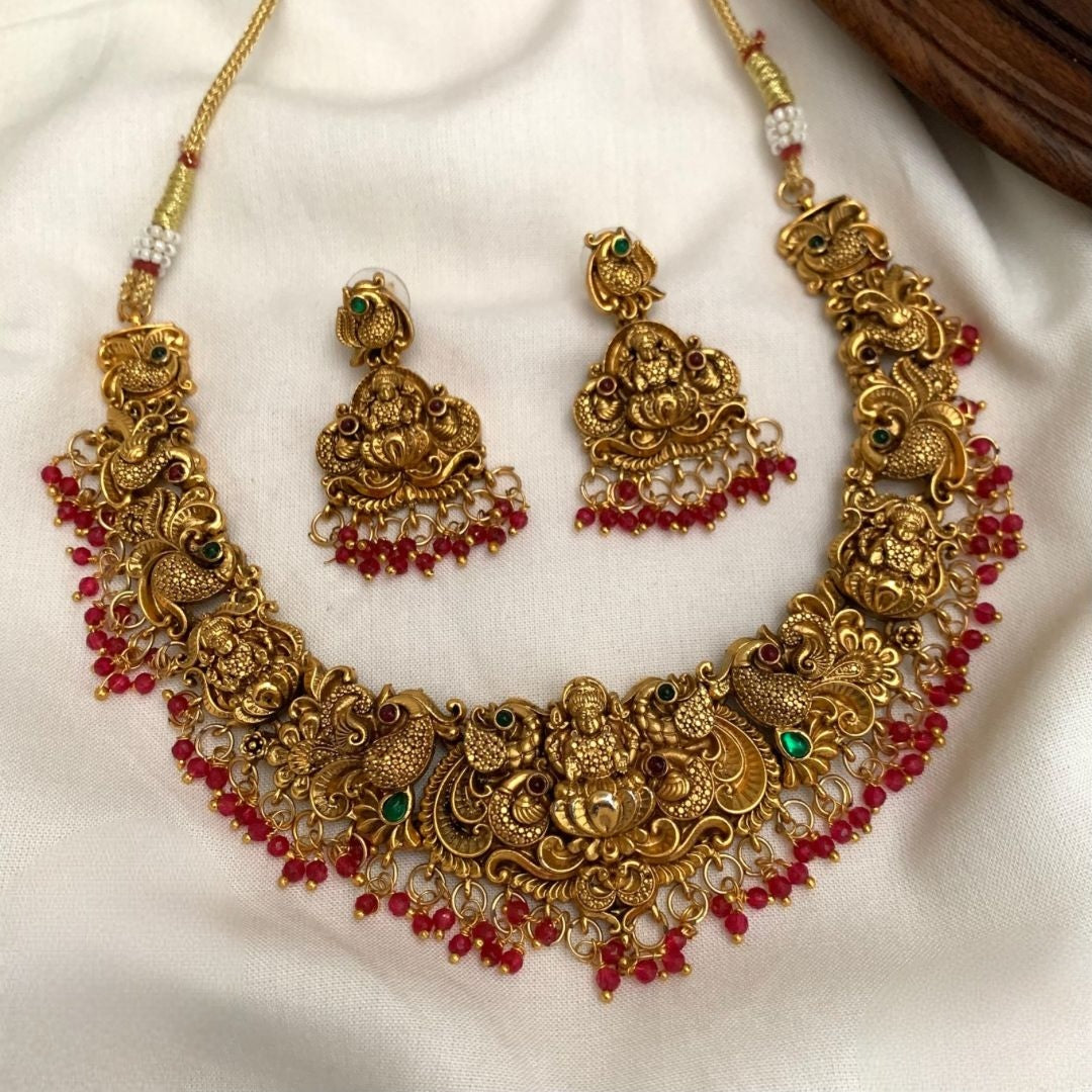 Premium temple jewelry necklace set features an intricate Goddess Lakshmi motif in an antique gold finish, accented with green/ruby beads and matching jhumka earrings product code T112