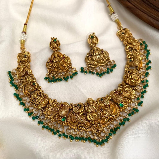 Premium temple jewelry necklace set features an intricate Goddess Lakshmi motif in an antique gold finish, accented with green/ruby beads and matching jhumka earrings product code T112