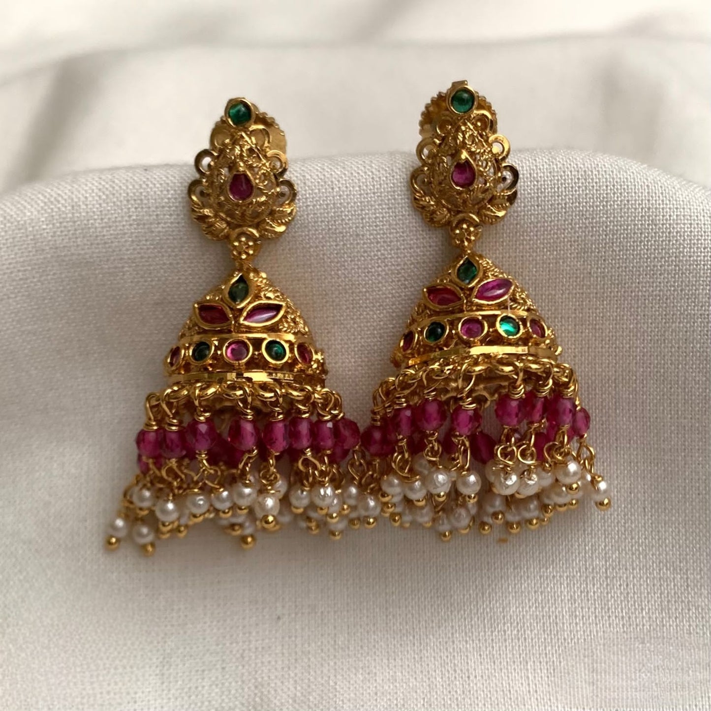 Premium antique-style gold-plated jhumki earrings featuring ruby and emerald stones, paired with dangling pink beads and white pearls code E141